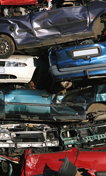 Pile de voitures épaves endommagées et de couleurs variées (violet, blanc, bleu, vert, rouge), empilées dans une casse automobile.